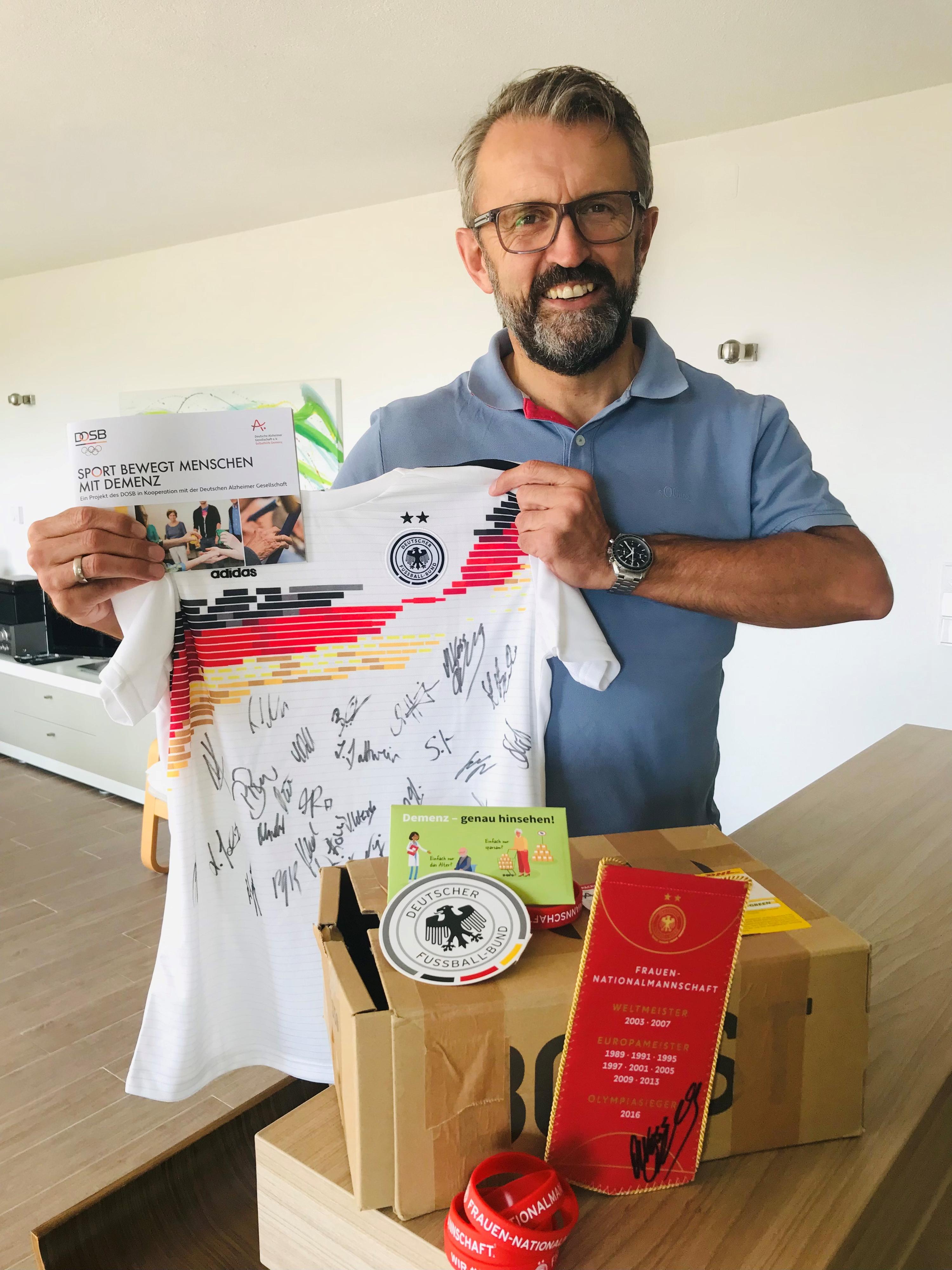 Der Gewinner Herr Andreas Kübler hält das unterzeichnete Trikot hoch und lächelt.