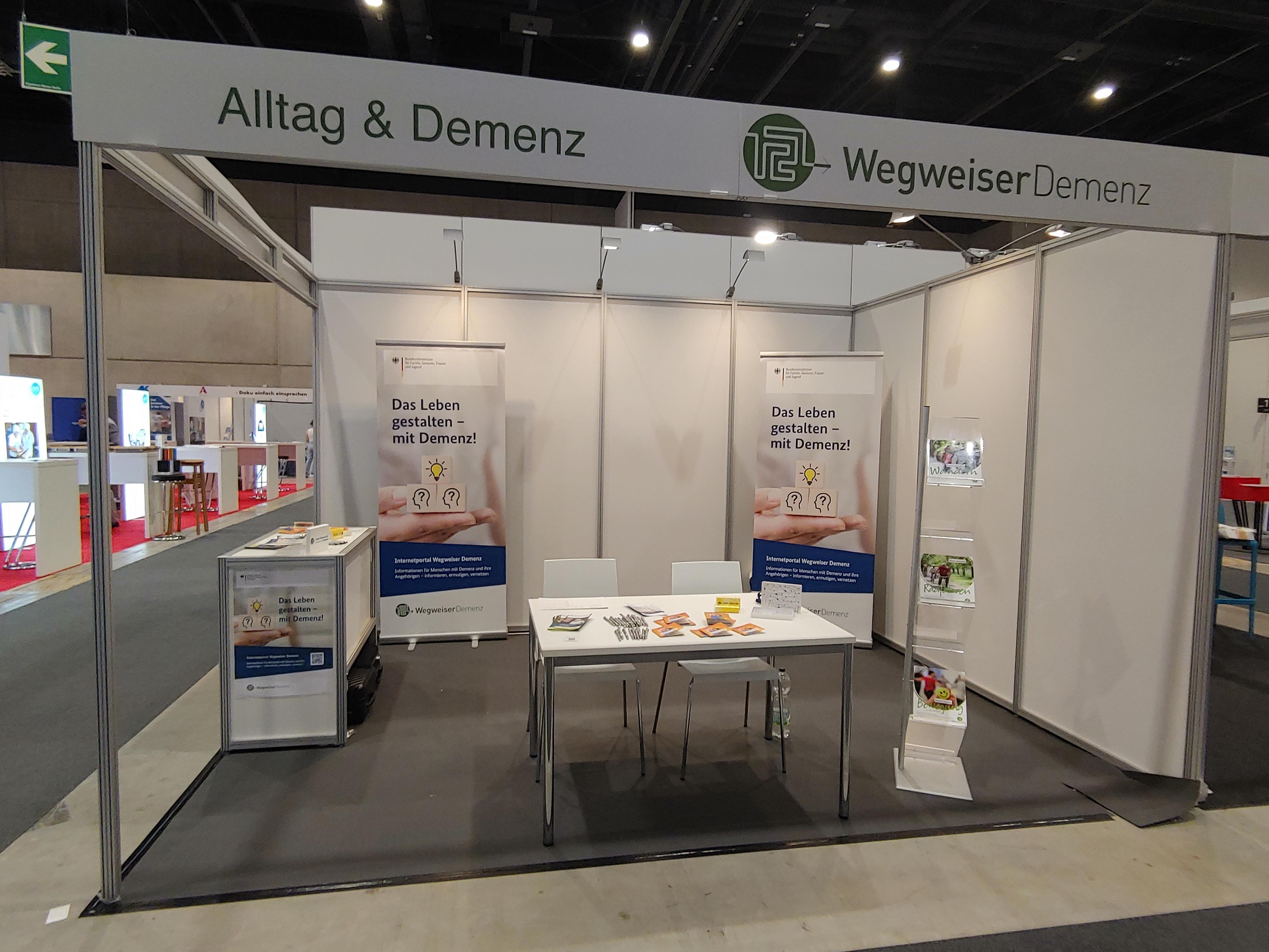 Ausstellerstand mit Tischen, Stühlen und Materialien wie Flyern oder Broschüren.