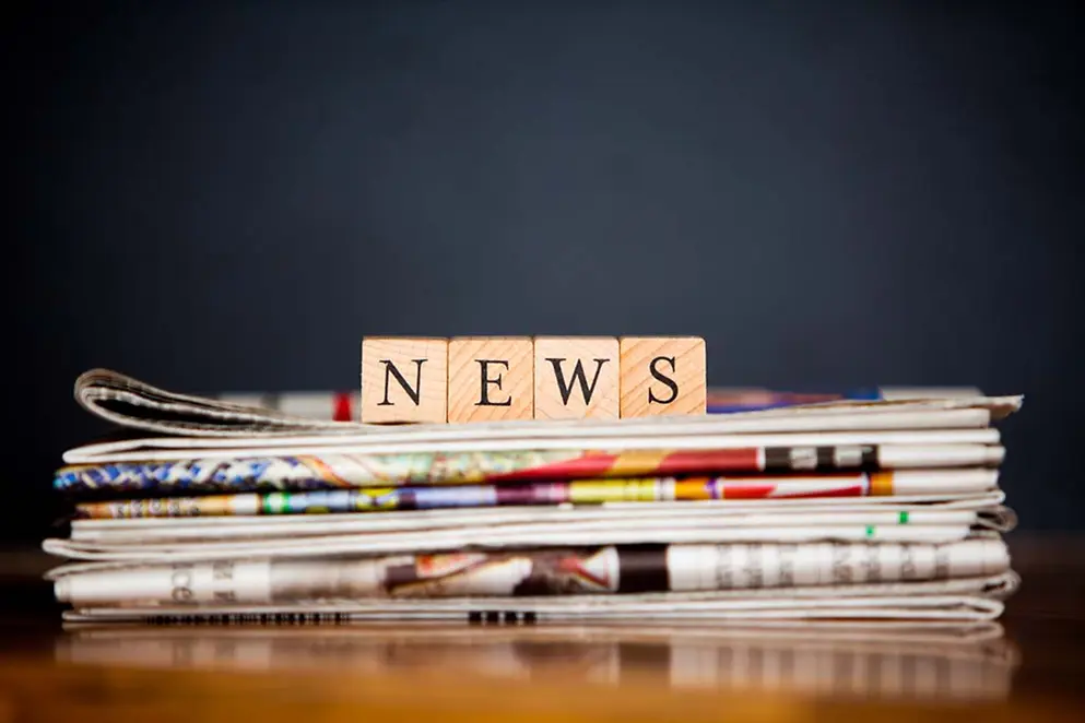 Ein Stapel Zeitungen mit Holzklötzen darauf, die das Wort News bilden.