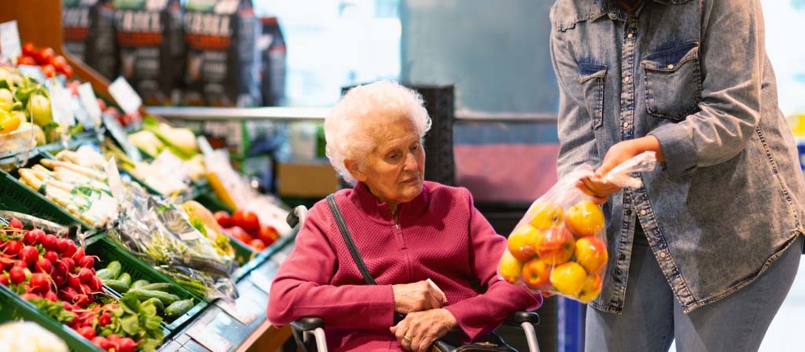 Eine junge Frau zeigt einer älteren Dame beim Einkauf eine Tüte mit Äpfeln.