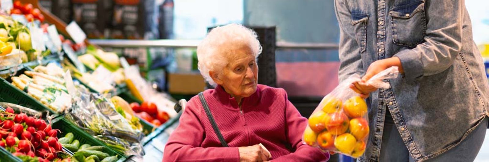 Eine junge Frau zeigt einer älteren Dame beim Einkauf eine Tüte mit Äpfeln.