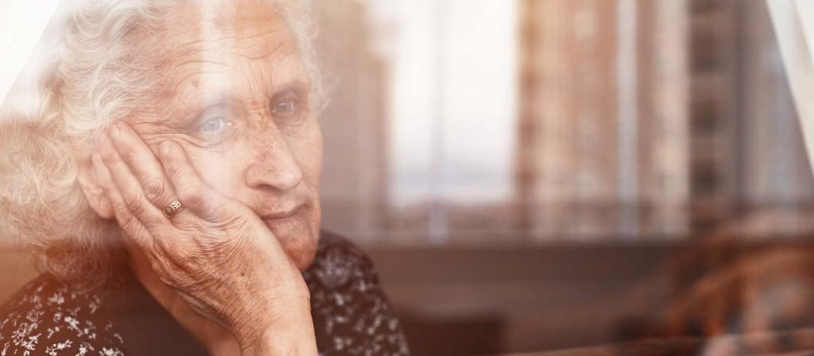 Eine ältere Frau sitzt allein am Fenster und sieht traurig nach draußen.