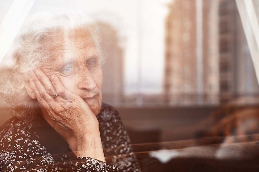 Eine ältere Frau sitzt allein am Fenster und sieht traurig nach draußen.