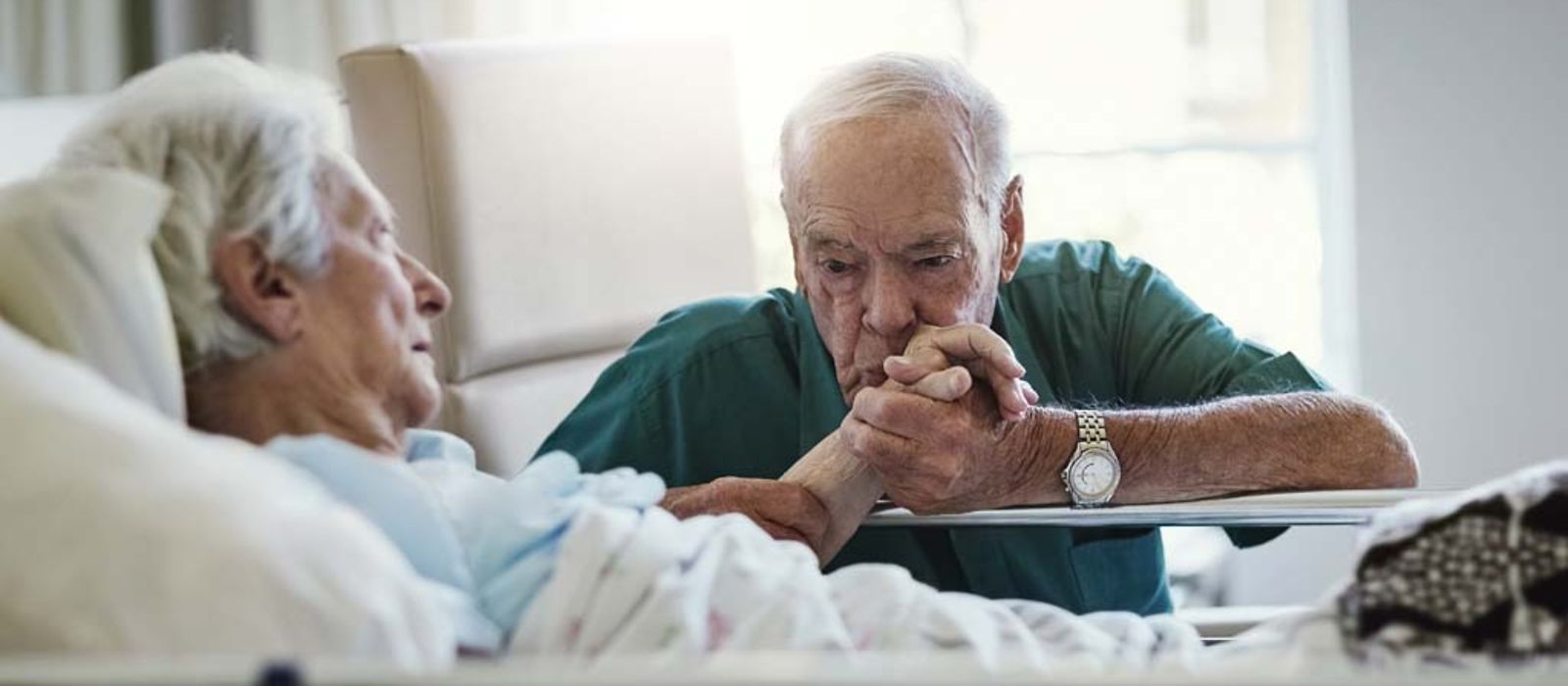 Ein älterer Mann küsst die Hand seiner Frau die Im Krankenhaus liegt.