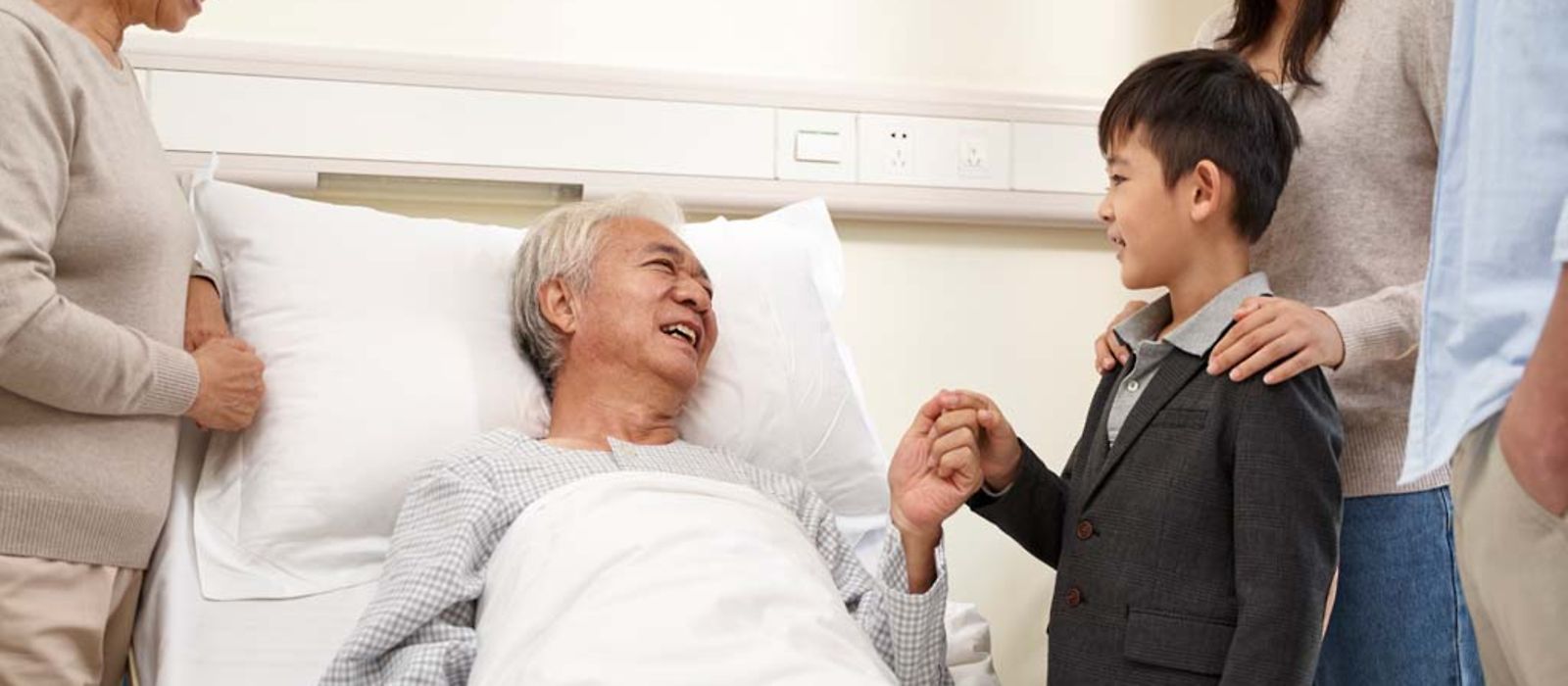 Ein Senior im Krankenhausbett hat Besuch von seiner Familie.