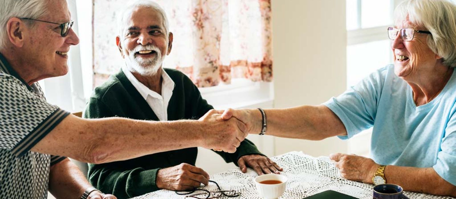 Drei Senioren sitzen zusammen am Tisch und begrüßen sich.