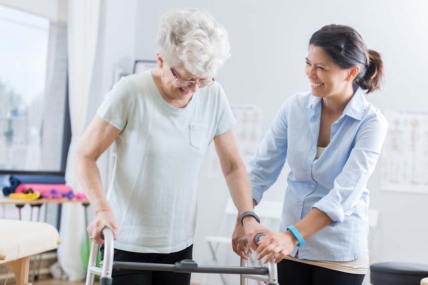 Medizinisches Fachpersonal hilft einer älteren Frau mit einer Gehhilfe zu laufen.