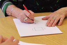 Eine ältere Dame zeichnet Quadrate aus ein Blatt Papier.