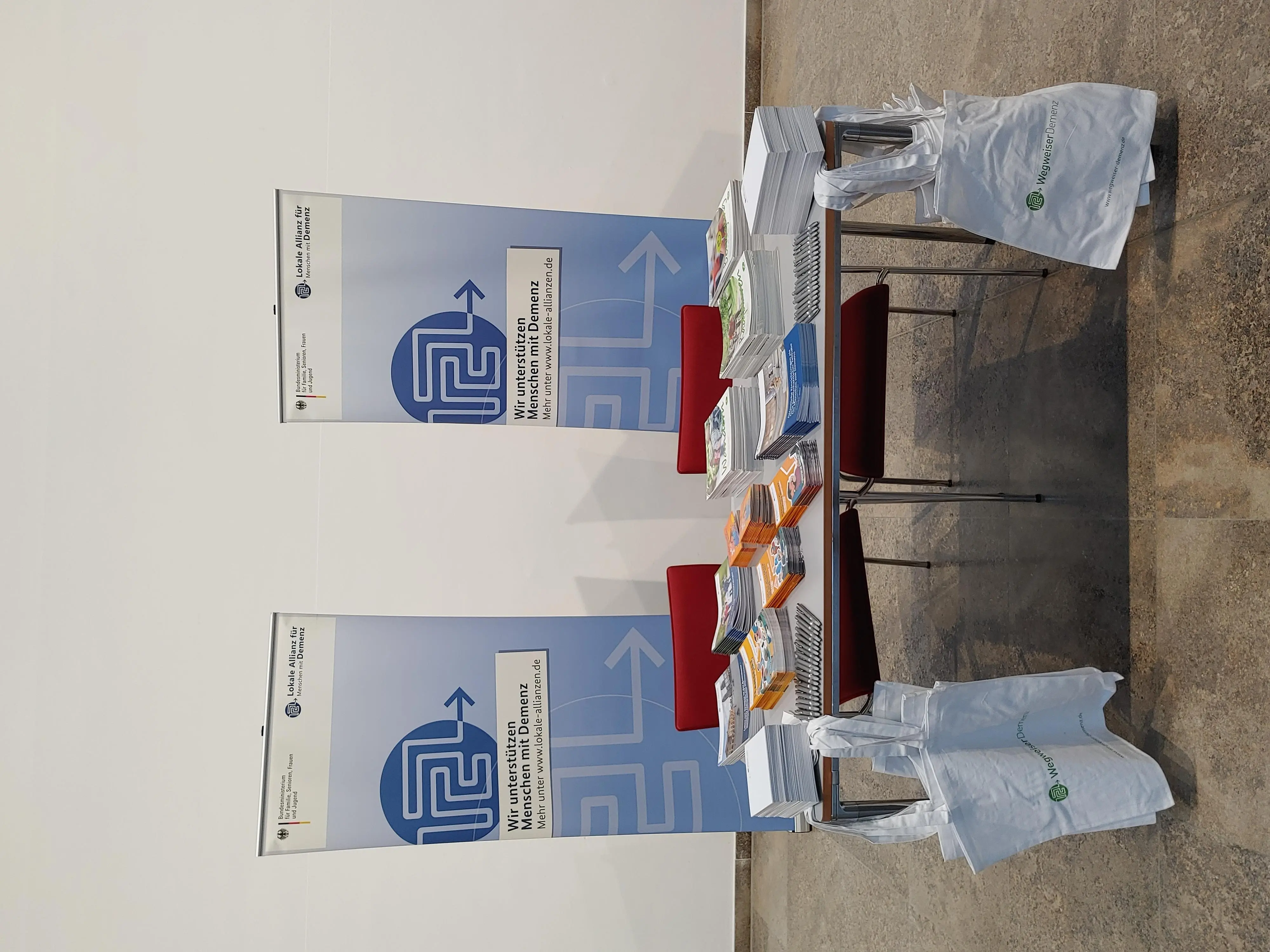 Ansicht des Ausstellerstandes mit einem Tisch, 2 Stühlen und diversen Broschüren auf dem Tisch.