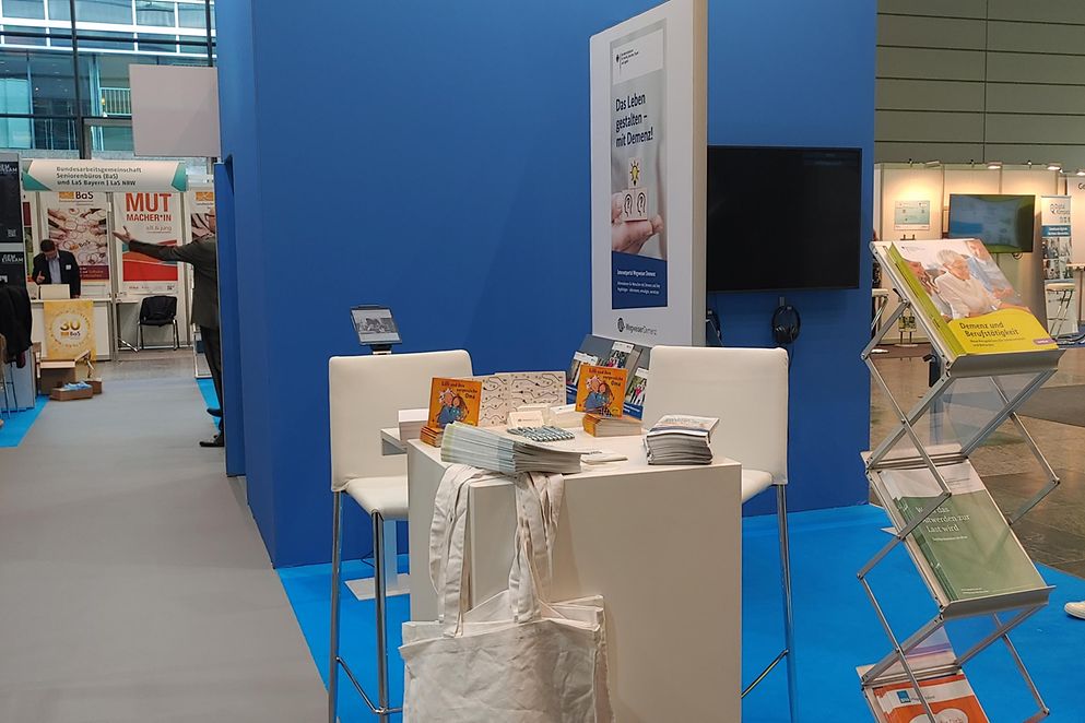 Abbildung des Ausstellerstandes mit einem Stehtisch, Barhocker und Broschüren.