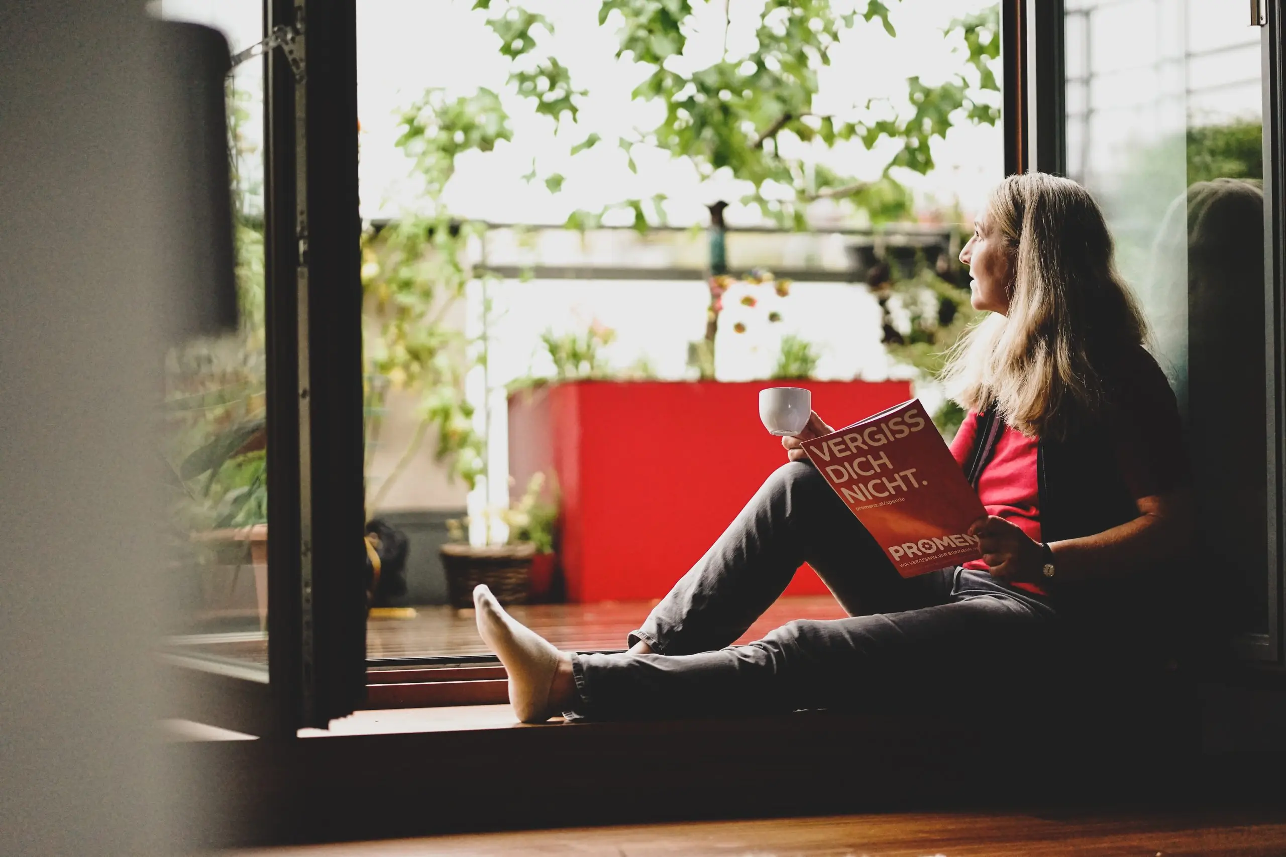 Eine Frau liest ein Buch und schaut aus dem Fenster.