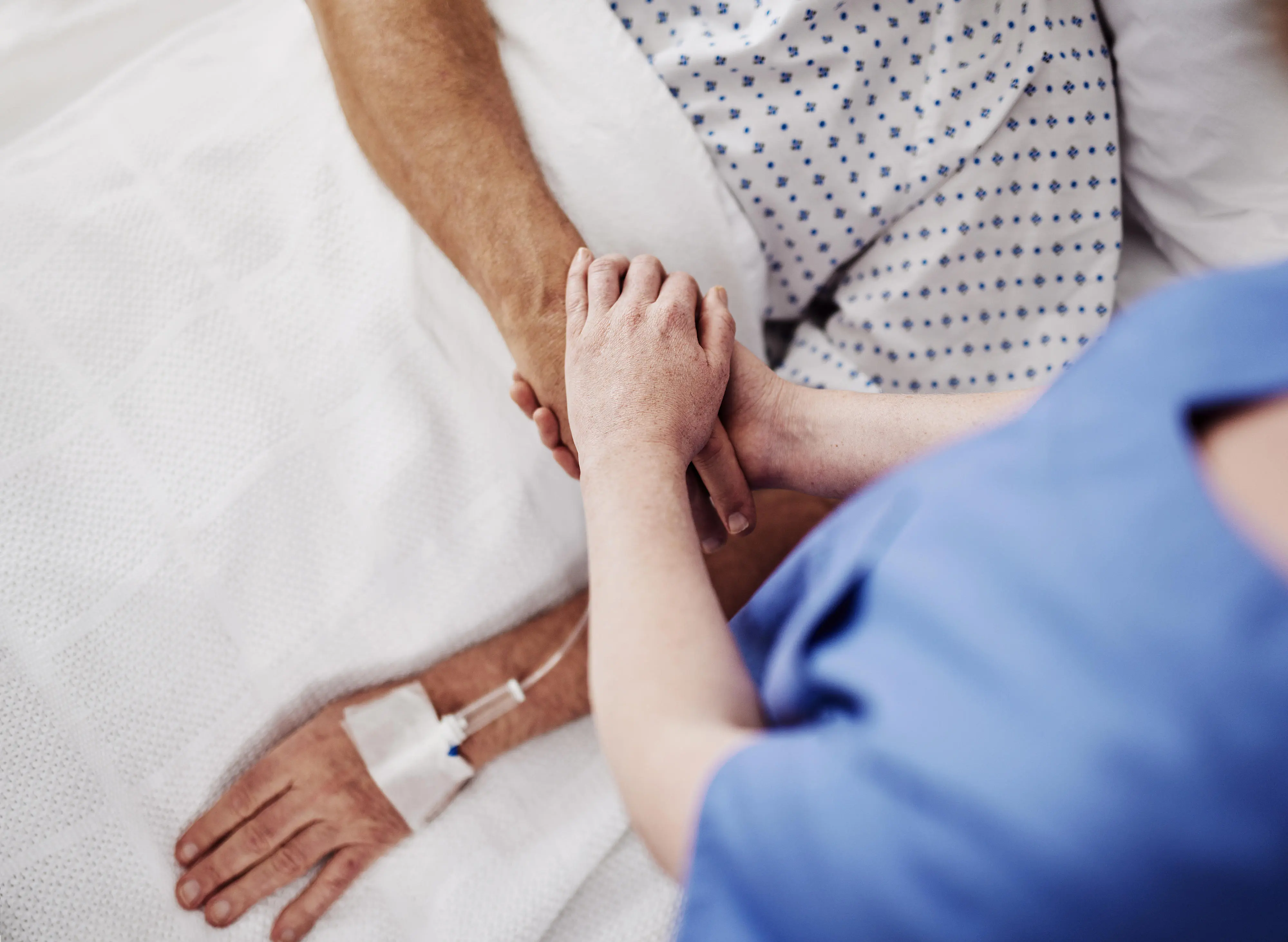 Eine Person hält die Hand einer anderen Person, die im Bett liegt.